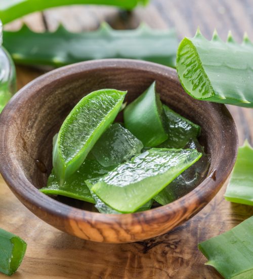 Fresh aloe leaves and aloe gel in the cosmetic jar on wooden table.